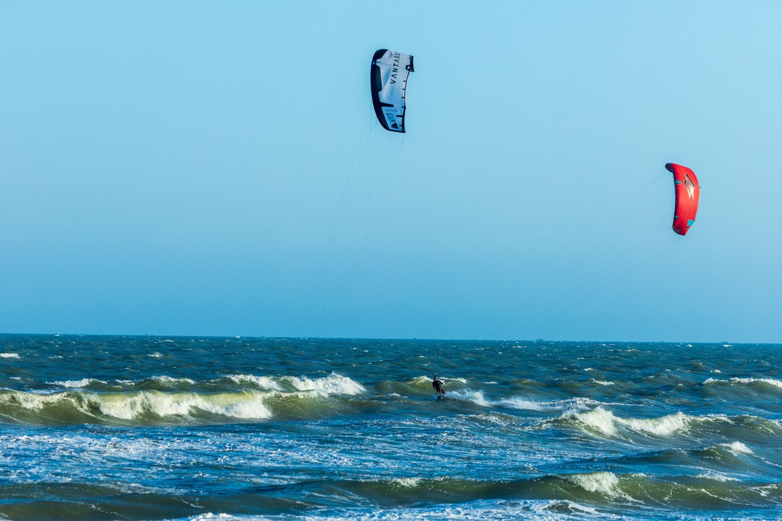 Kitesurfer enjoying thrilling ride on open ocean waves under blue sky.